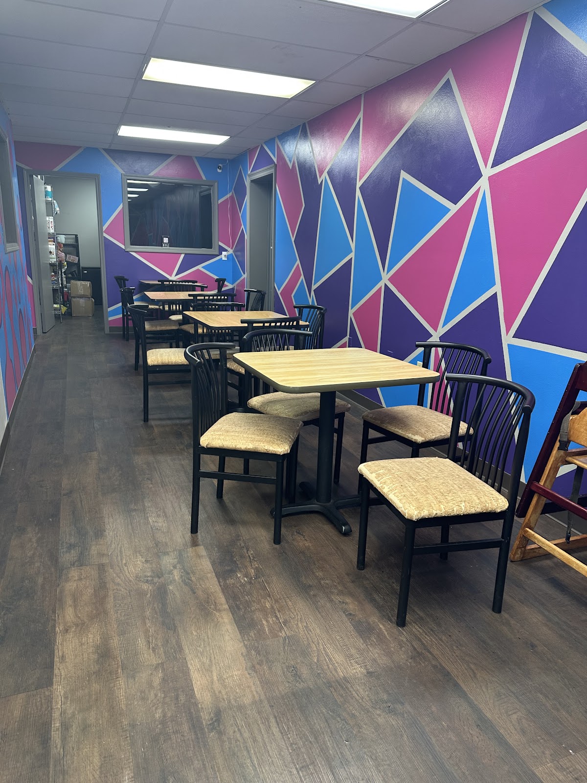 Tables and black chairs beside Suki’s pink, purple and blue geometric wall.